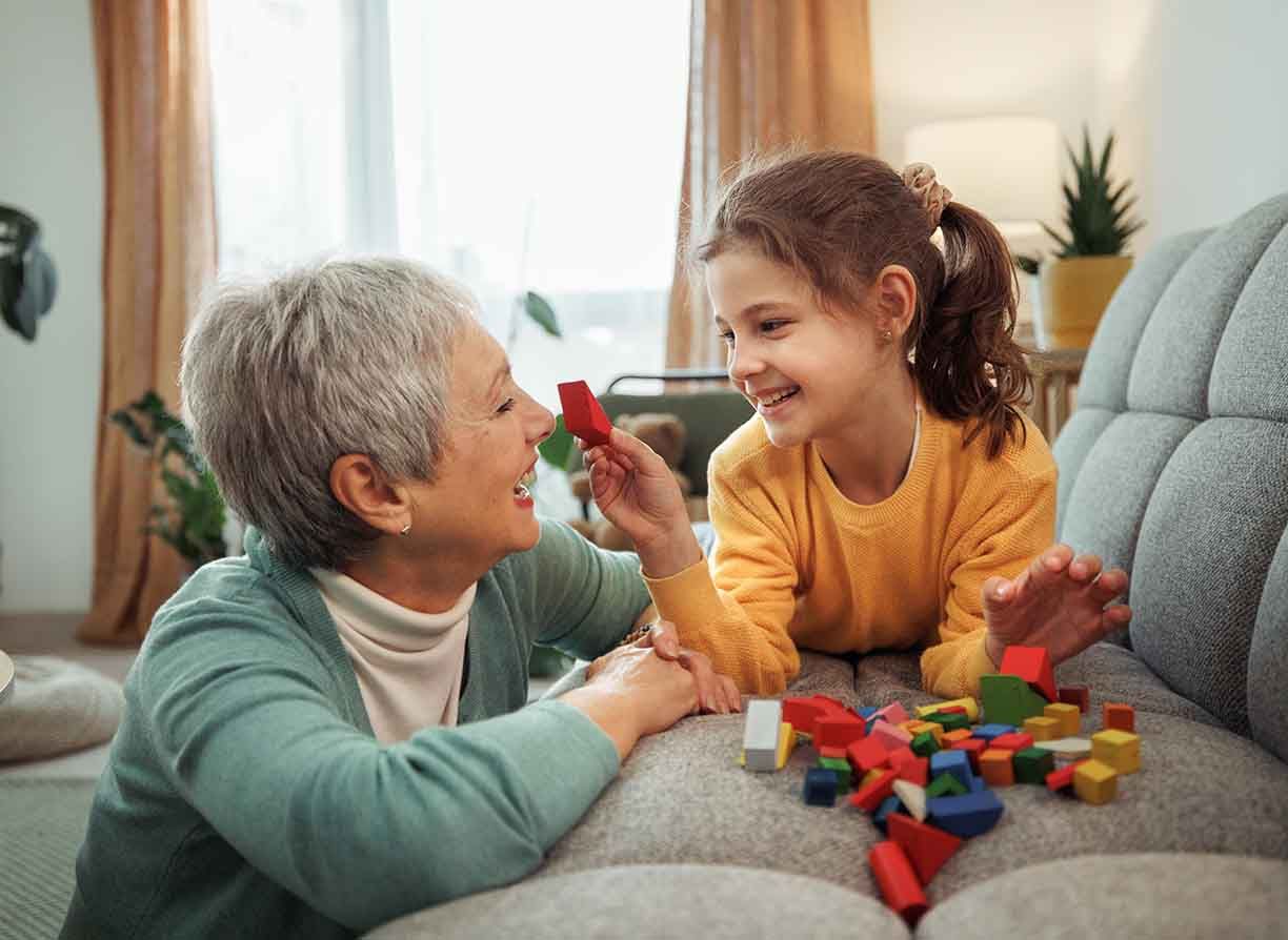 Grandmother and granddaughter enjoy playful moments together, building with wooden toy blocks in their home