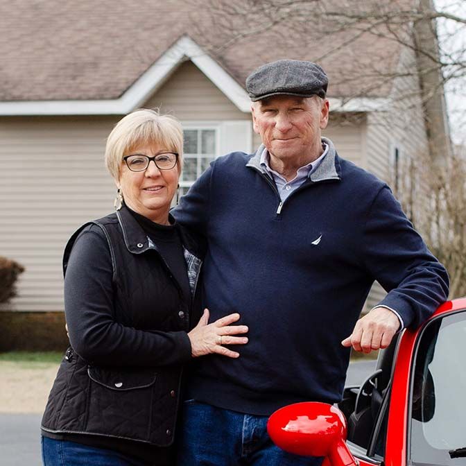 Retired couple poses next to their red convertible