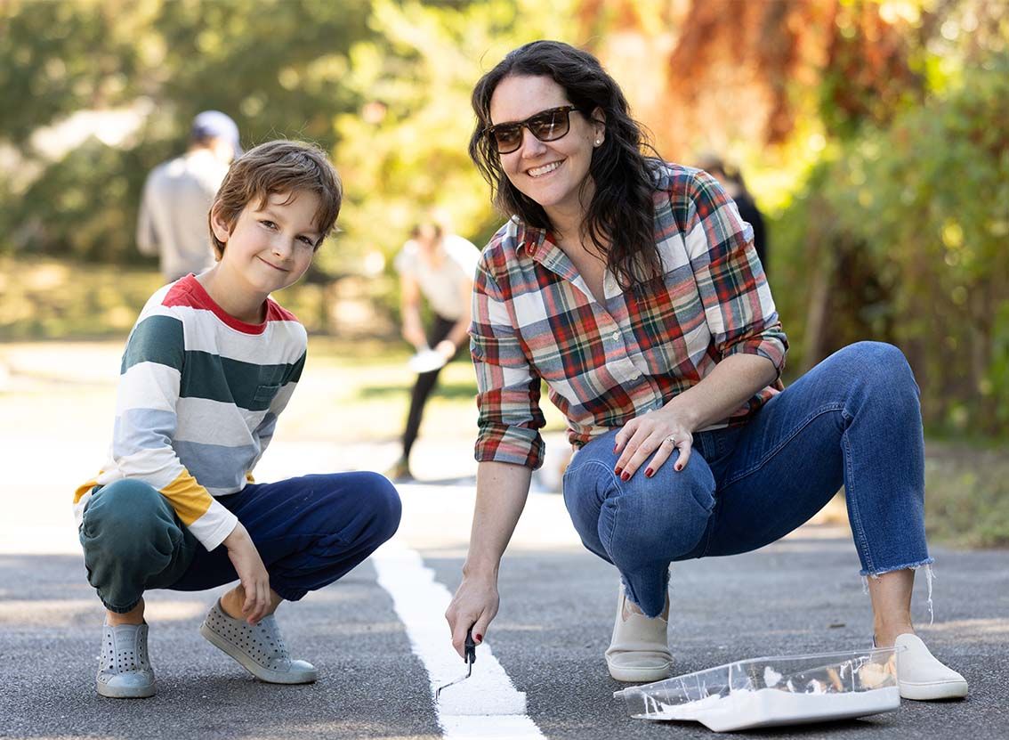 A mom and her son help paint lines on a road