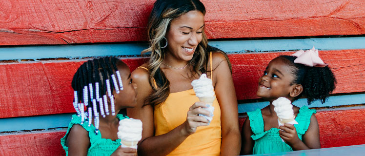 A mother and two daughters smiling while eating ice cream