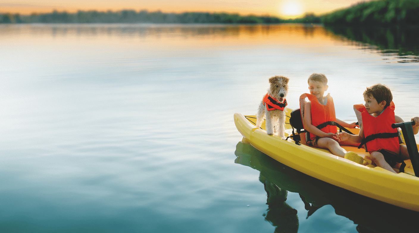 Two boys canoe with their dog on a calm lake at sunset